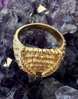 A top view of the Athena Owl Ring, displaying the feather detailing, and thickness of the band. Against an amethyst crystal background.