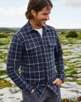 A man wearing a Faherty Legend Sweater Shirt in Low Rider Blue long-sleeved blue flannel shirt with a plaid navy,grey, and white buttoned collar, and front pockets.