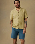 Man wearing a light green shirt and blue shorts against a beige background