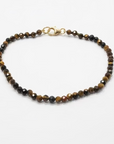 A brown and black beaded Tiger's ye bracelet, with a small gold-filled clasp. Against a white background.
