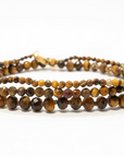 Three Tiger's Eye bracelets stacked on top of each other to show the varying sizes. Large beads are on the bottom, medium in the middle, and dainty on the top. Against a white background.