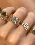 A hand showcasing many different JNB Style gold vermeil rings, with a hammered band on the pointer finger.