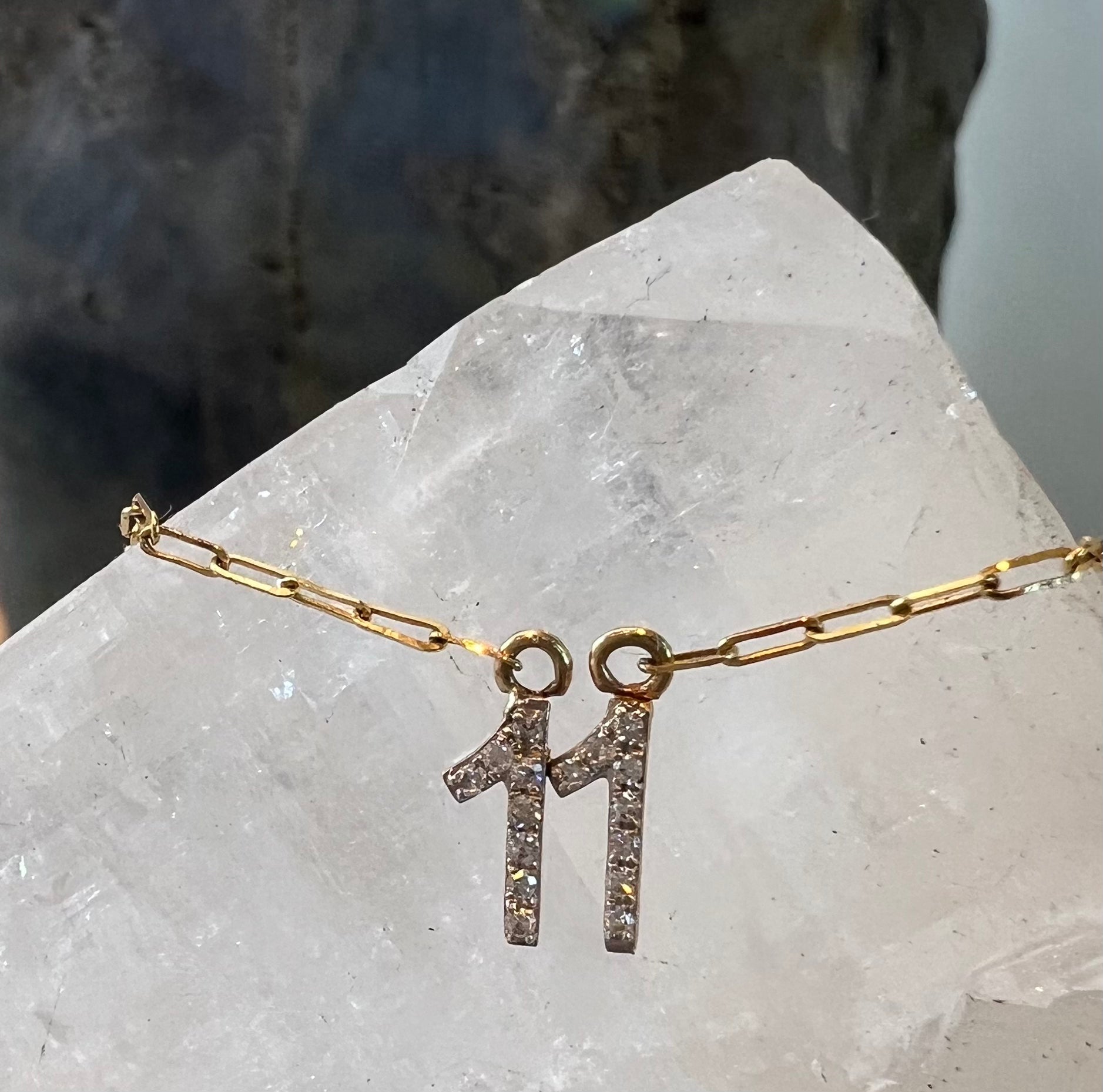 A close up detailed photo of the 11 diamond pendant, attached to a paperclip chain. In the background is a white quartz crystal.