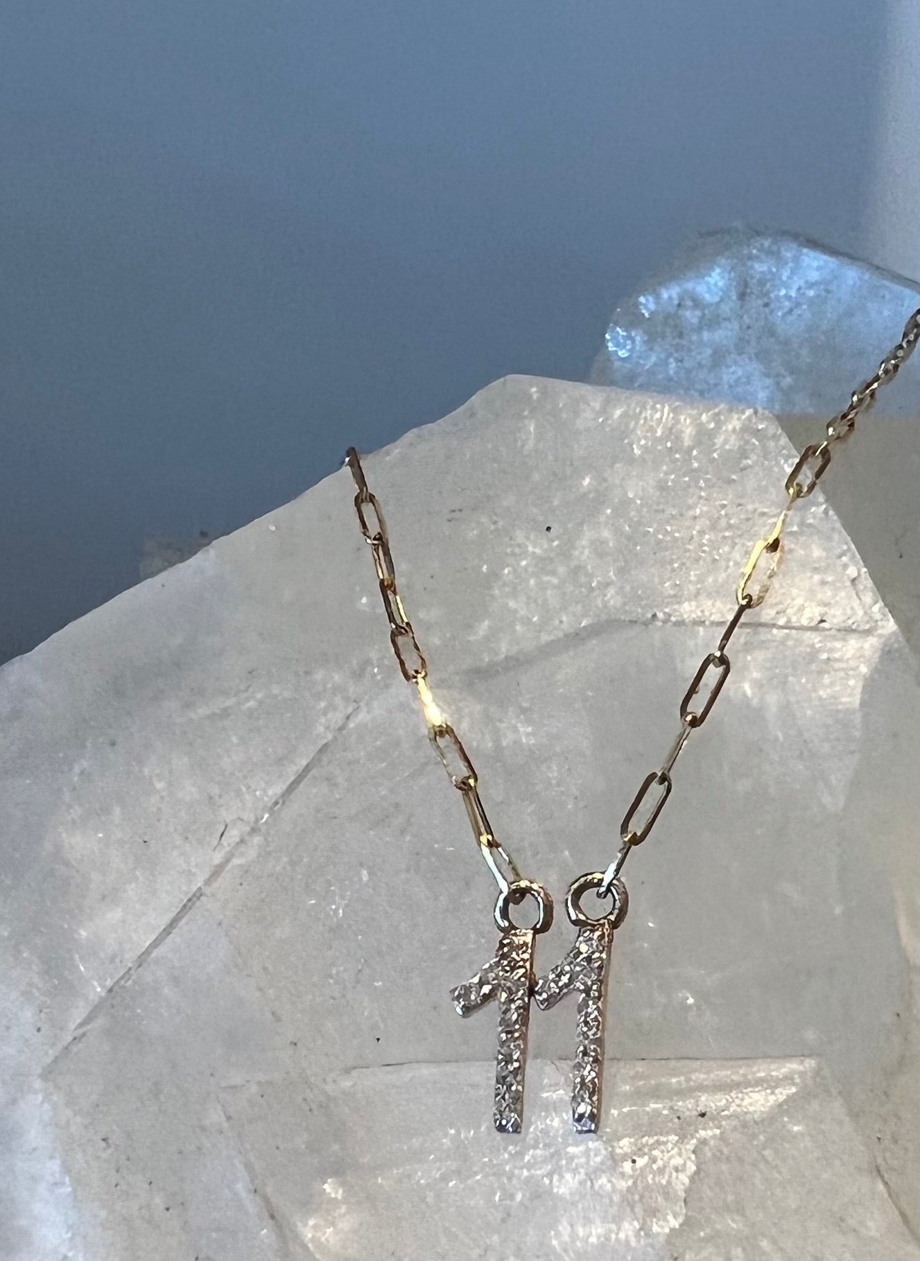 11 diamond pendant on a solid 14k gold paperclip chain, set against a white quartz crystal.