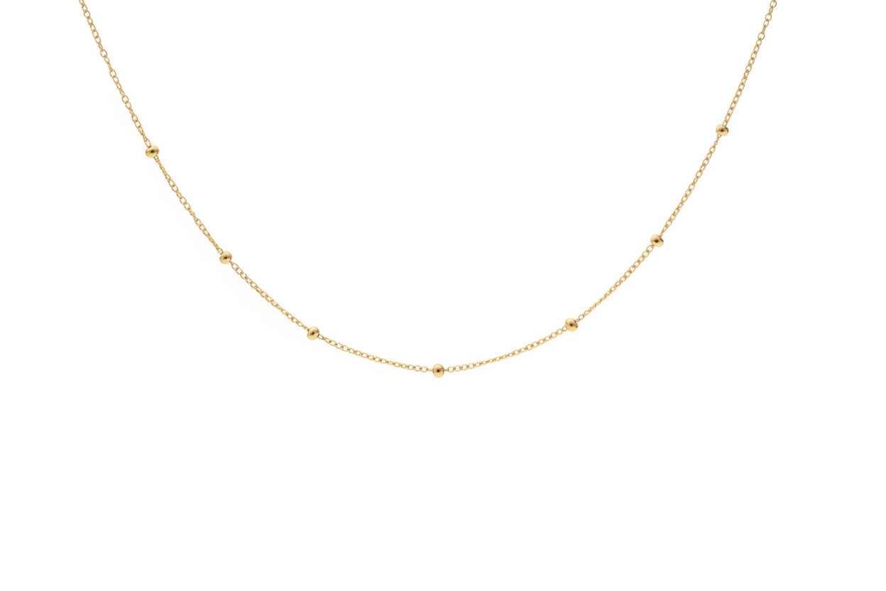 Solid 14k yellow gold station ball chain necklace on a textured stone surface