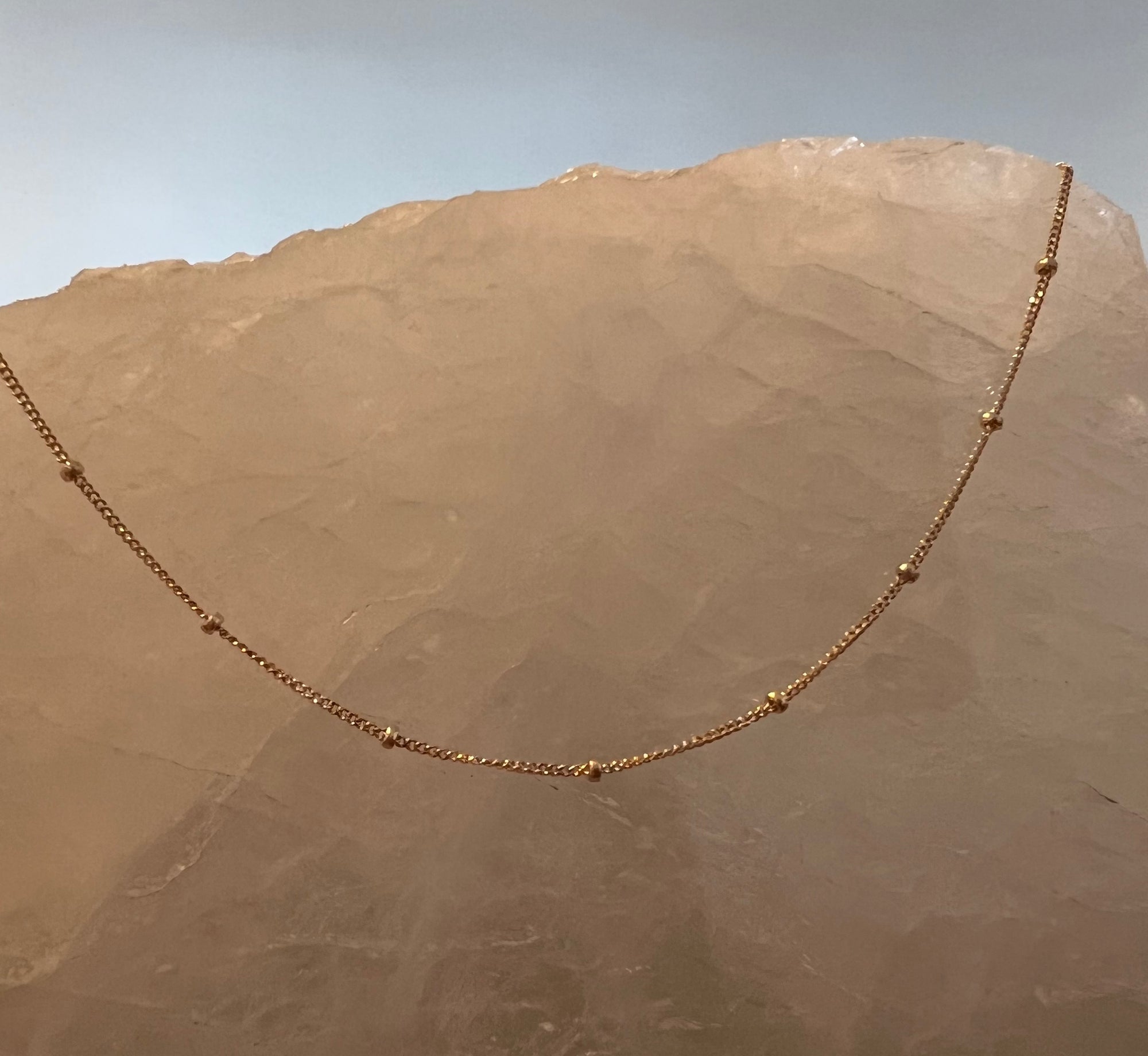 Solid 14k yellow gold station ball chain necklace on a textured stone surface