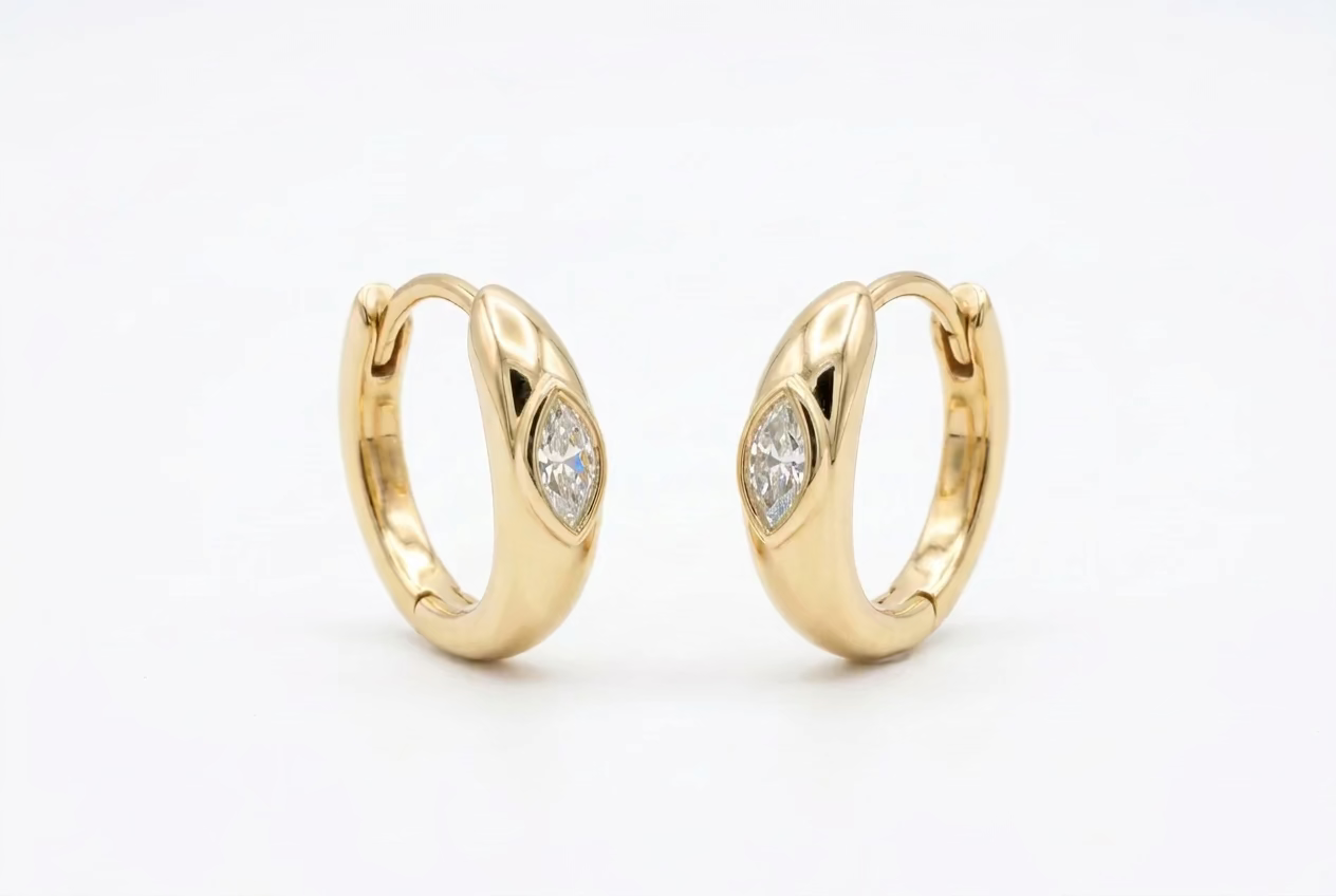 Solid 14k yellow gold huggies, with a bezel set marquise diamond, against a white background.