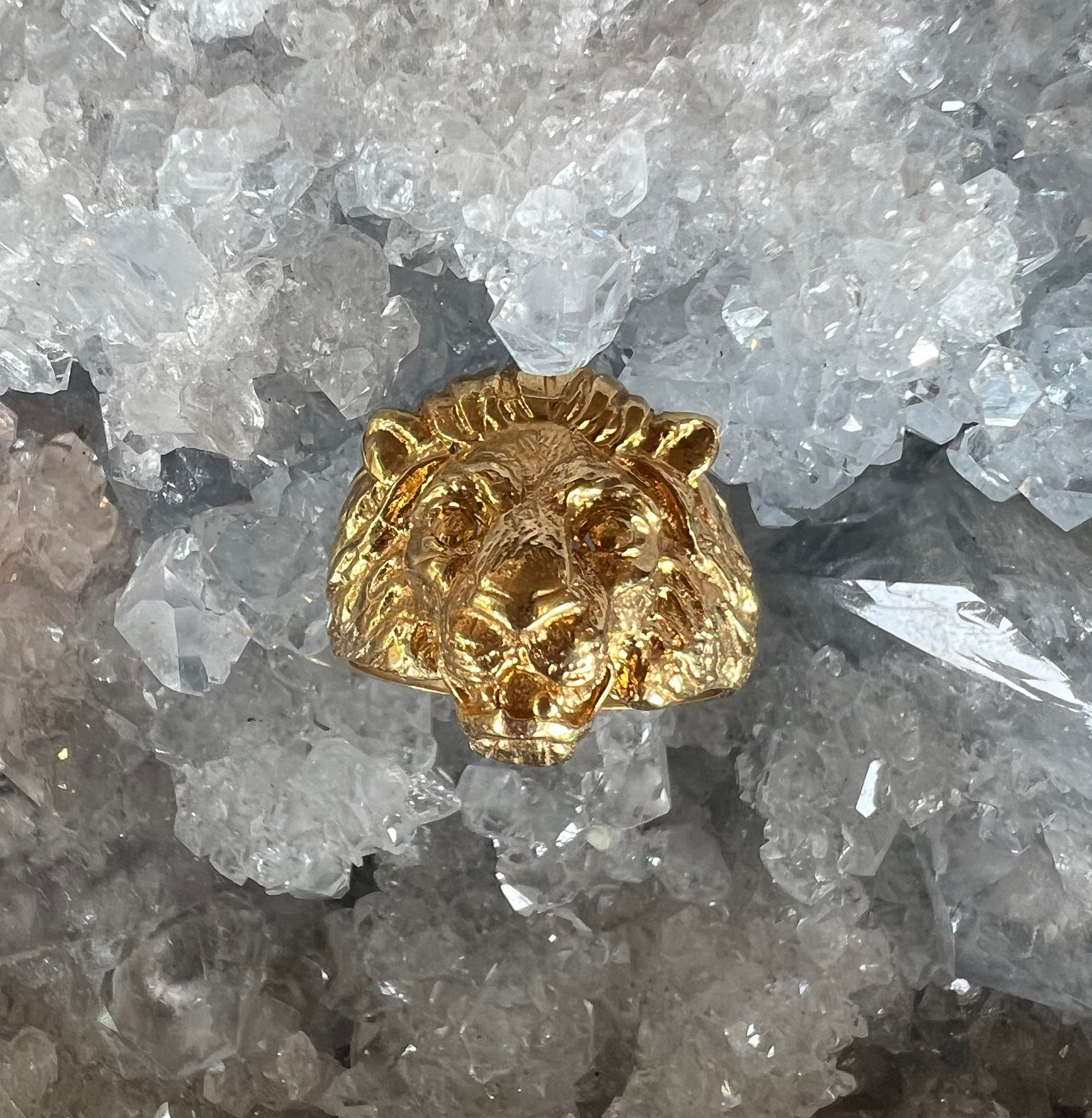 Front view of the face of the lion in the Aslan King of Beasts Gold Vermeil Lion ring. Showing the detail in the face and mane, and powerful gaze. Against a crystal background.