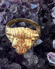 The top view of the Aslan King of Beasts Gold Vermeil Lion Ring. Showing the thick band, and detailing with the lions furrowed brow and mane. Against an Amethyst crystal background. 