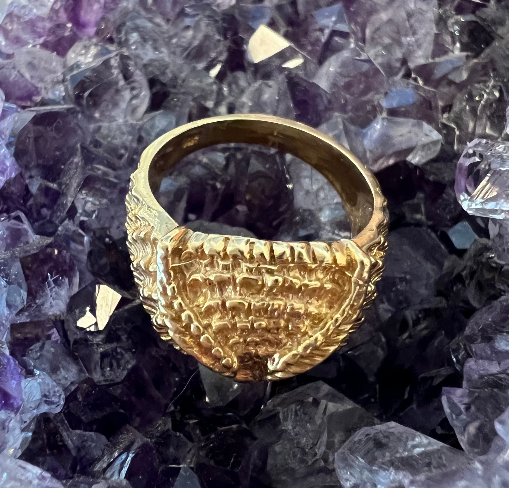 A top view of the Athena Owl Ring, displaying the feather detailing, and thickness of the band. Against an amethyst crystal background.