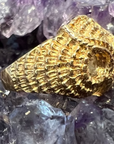 A side view of the Athena owl ring, showing off the feather detailing going around the sides, as well as the feathered eye feature. Against an amethyst crystal background. 