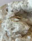 A solid 14k gold band with multiple brilliant cut diamonds set in bezel settings, with pave diamonds in between, creating a unique diamond band. Displayed on a bed of white crystals.