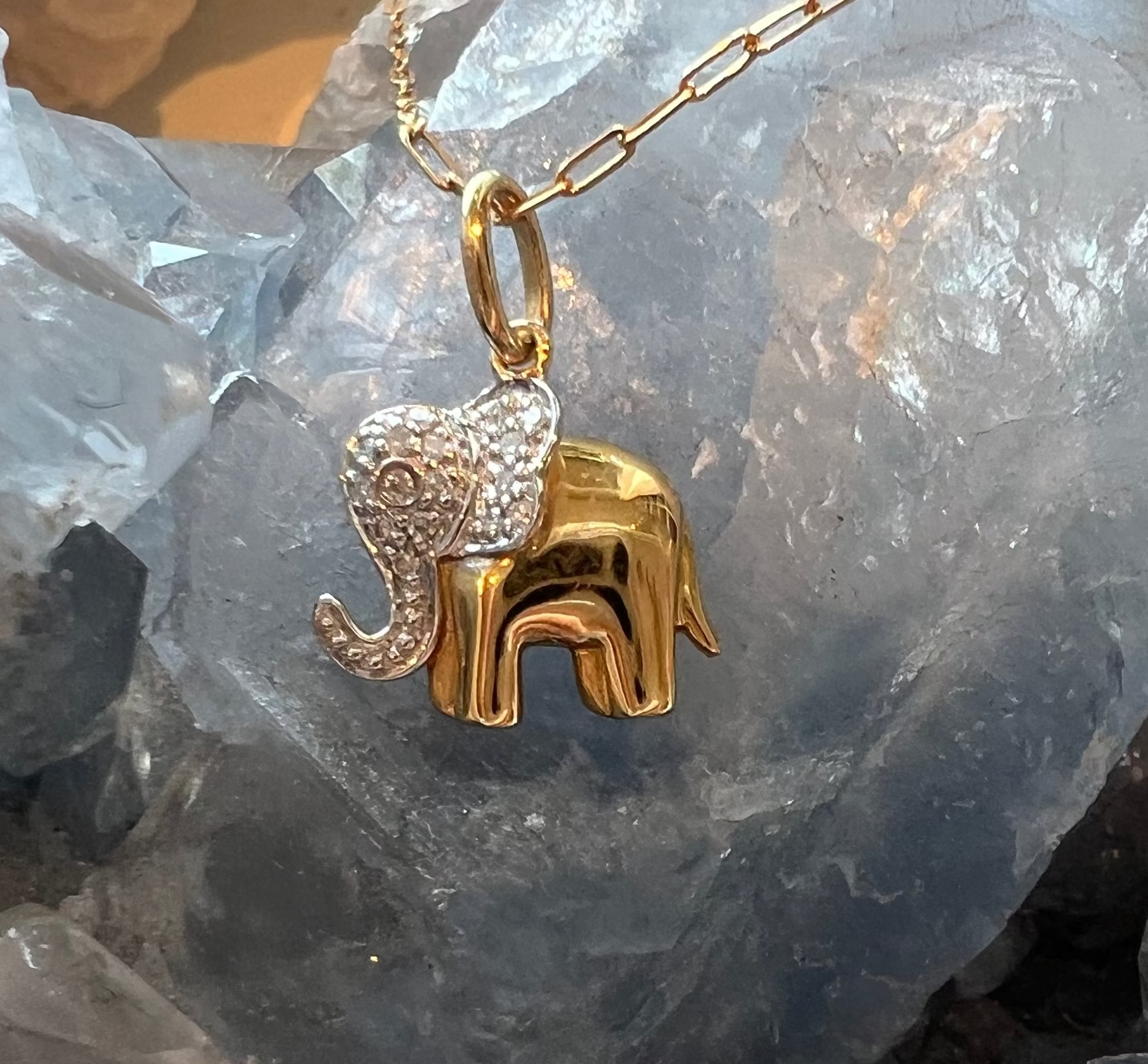 14k gold elephant pendant with pave diamonds on a paperclip chain on a crystal background