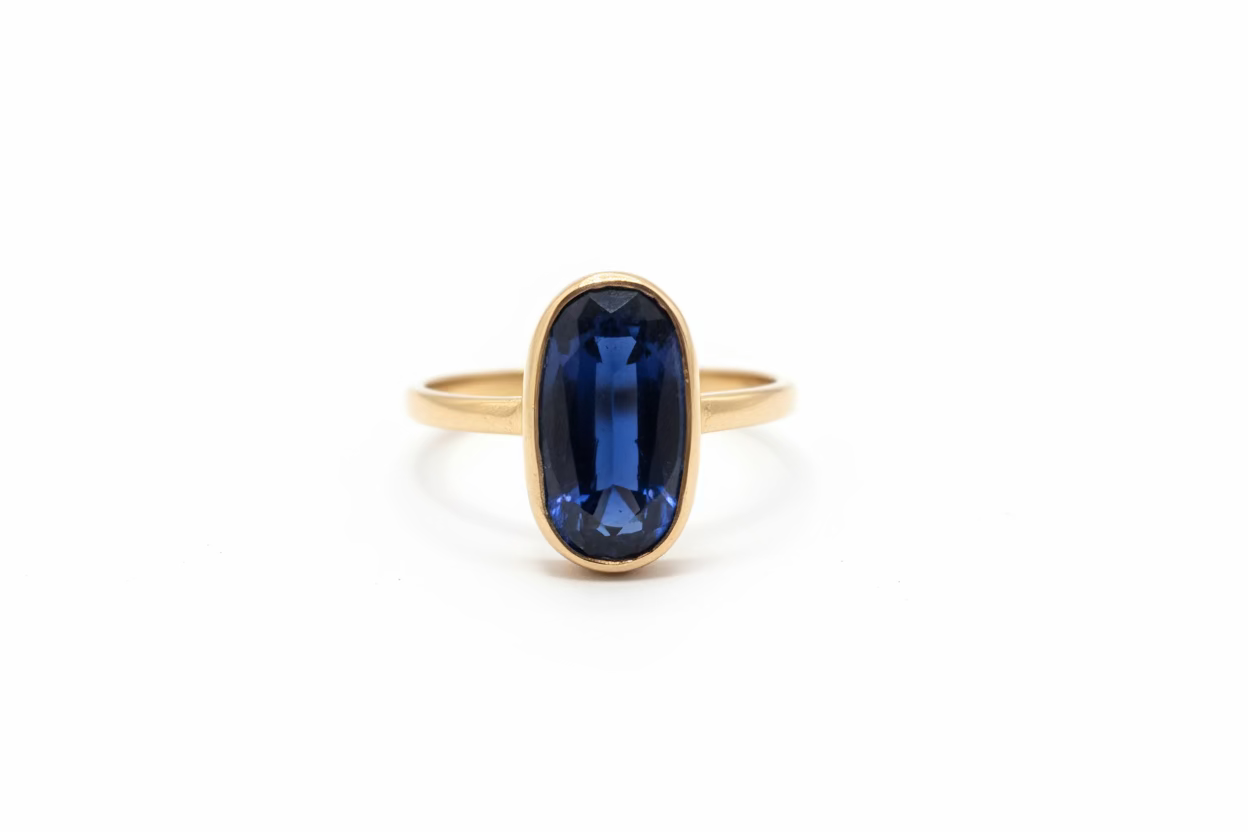 A 14k yellow gold ring with a large oval dark blue kyanite gemstone, displayed with a white background. 