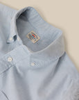 Close-up of a light blue and white micro-striped button-down shirt collar, showing the 'FAHERTY' brand label inside the neck, set against a solid beige background.