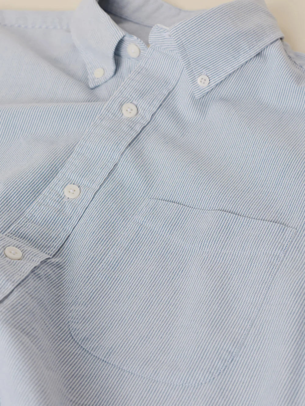 Close-up of a light blue and white micro-striped organic cotton button-down shirt with a single chest pocket and white buttons.