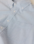 Close-up of a light blue and white micro-striped organic cotton button-down shirt with a single chest pocket and white buttons.