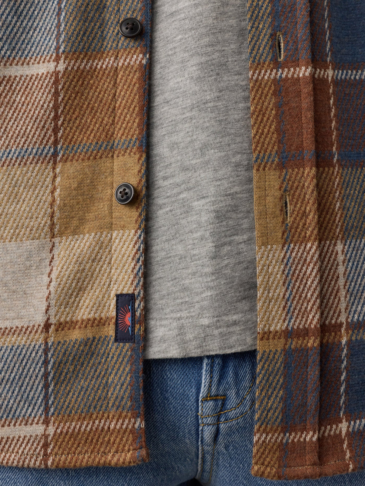 A detailed shot of the hem and buttons of the faherty boulder creek plaid shirt, which is beige, red, white and light blue plaid button down. 
