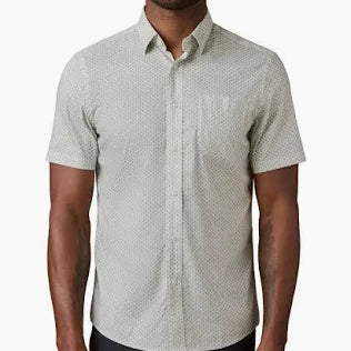 A man wearing a green sea shell patterned short-sleeve shirt on a white background.