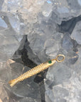 Solid 14k gold fish-shaped pendant with a green emerald gemstone eye on a crystal background