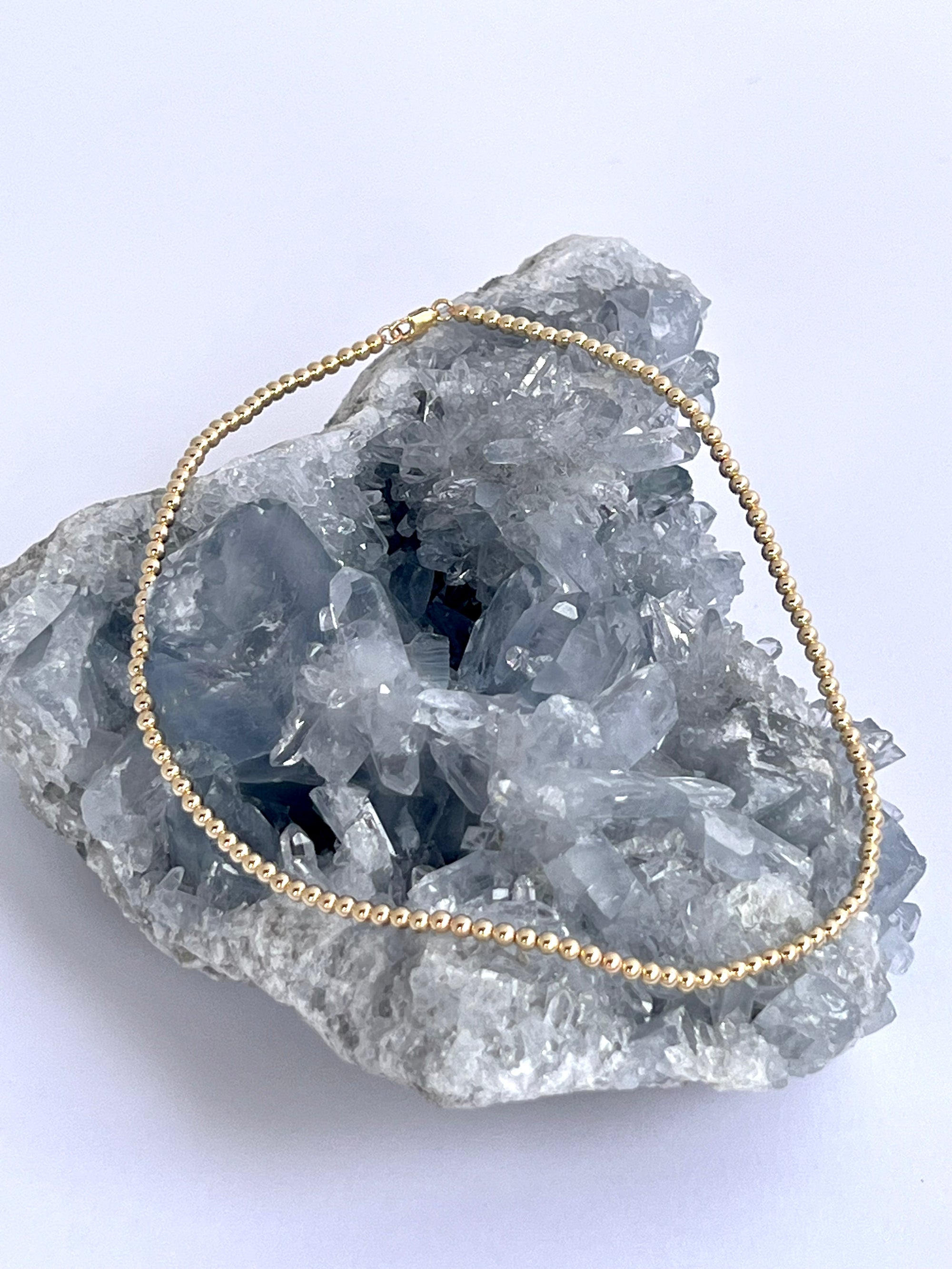 A 14k gold filled ball chain necklace, displayed on a crystal.