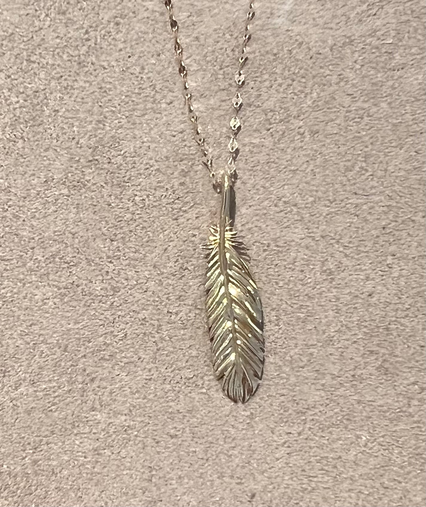 Solid 14k Gold Feather pendant on a delicate disc chain, with a beige background