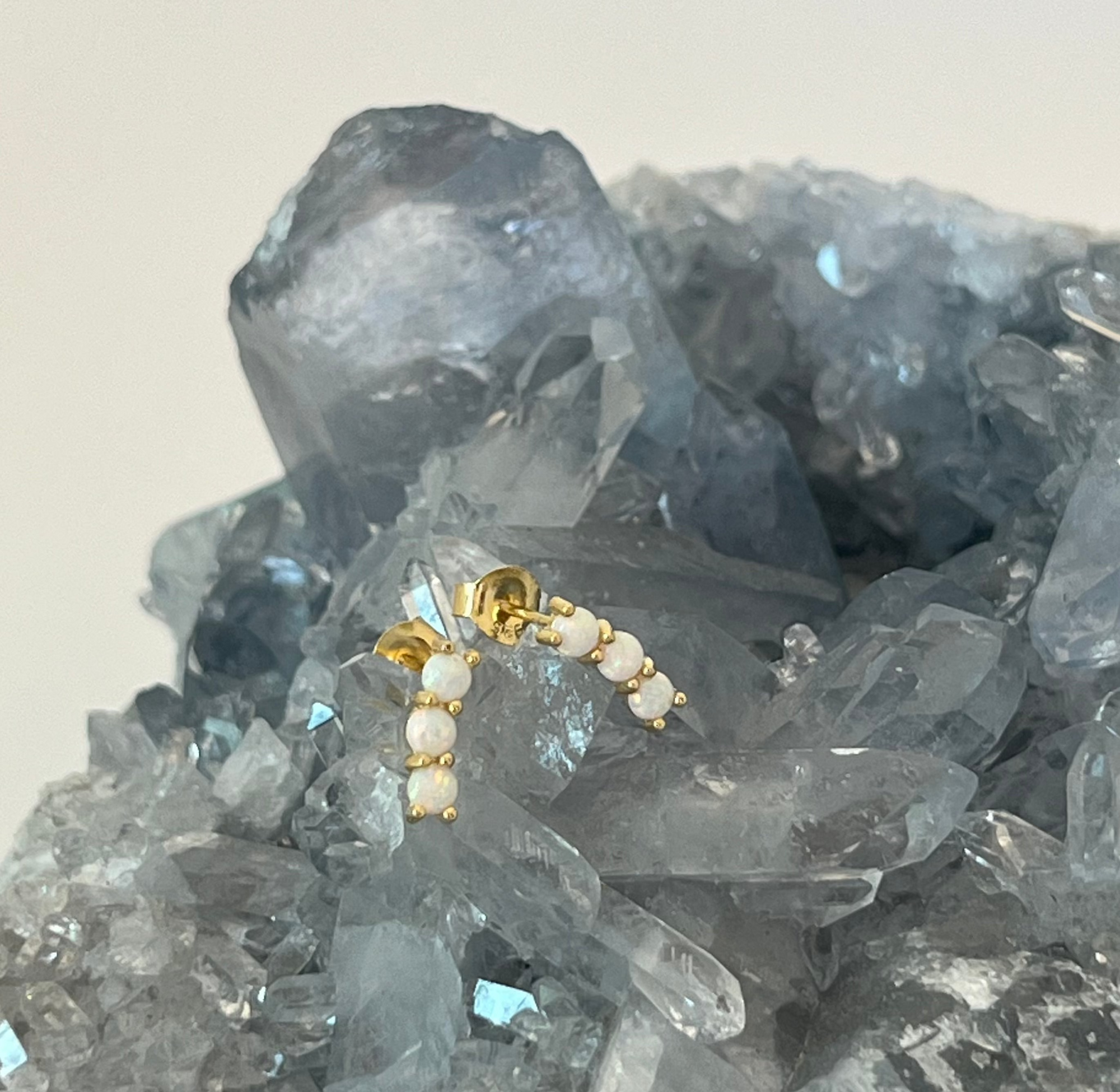 Gold vermeil stud earrings with three opals in a celestial arc shape, displayed on a crystal.