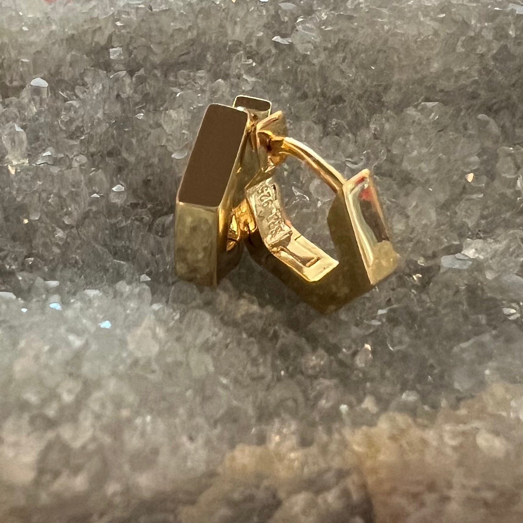A pair of gold vermeil hexagon hoop earrings, displayed on a textured gray crystal surface.