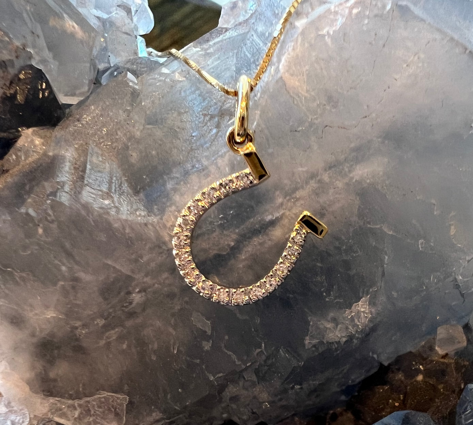Solid 14k Yellow Gold Horseshoe pendant with 18 VS1 Diamonds in a pave setting. With a gold box chain, against a celestite crystal background. 