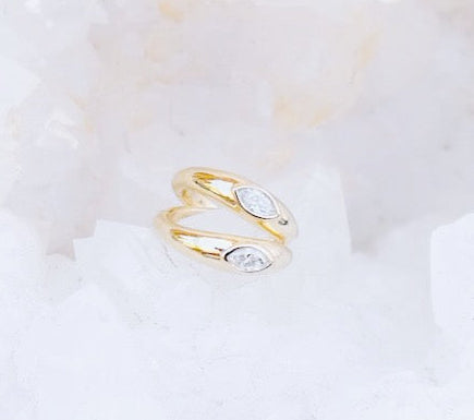 A pair of elegant Marquise Diamond Huggies earrings. The earrings are characterized by their sleek, minimalist design, with each earring featuring a single marquise-cut diamond elegantly set.