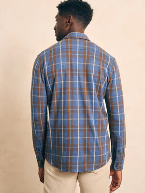 The back of a man wearing a Faherty Legends Sweater Shirt in Alpine Lake Plaid in blue and brown colors, against a beige background. 