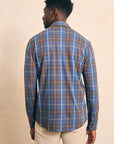The back of a man wearing a Faherty Legends Sweater Shirt in Alpine Lake Plaid in blue and brown colors, against a beige background. 