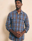 A man wearing a long-sleeved Faherty Legends Sweater Shirt in Alpine Lake Plaid shirt in blue and brown colors with a buttoned front and two chest pockets.