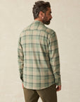 Back of a man wearing Faherty's  Forest Drive Plaid long-sleeve button down shirt in varying shades of green, against a beige background. 