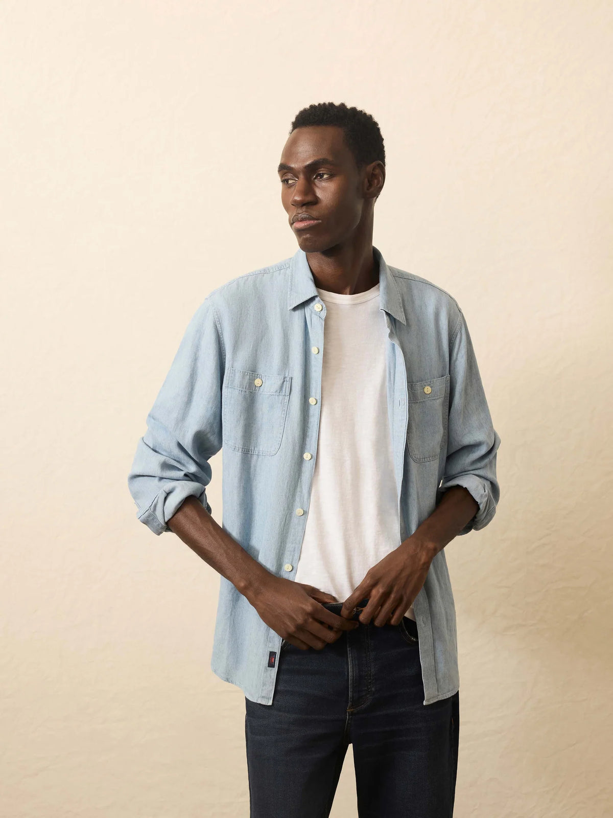 Man wearing a light blue denim shirt over a white t-shirt on a beige background