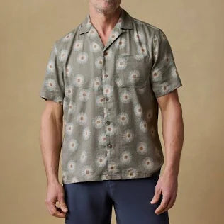 A man wearing a green with firework patterned shirt against a beige background.