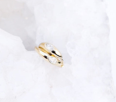 A pair of solid 14k yellow gold huggies, featuring a singular bezel set diamond, against a white background.