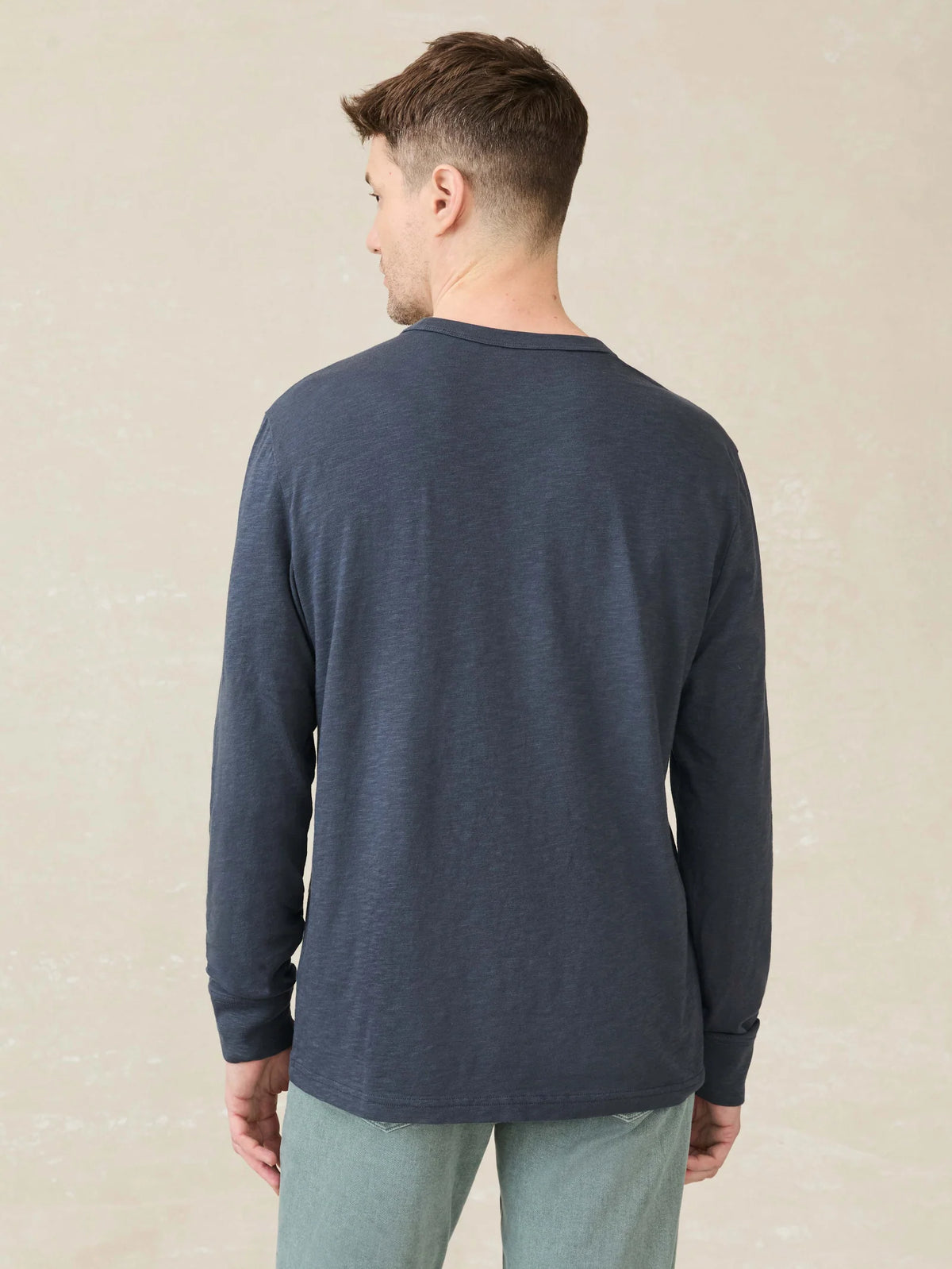 A man wearing a Faherty navy blue long-sleeve shirt against a beige background