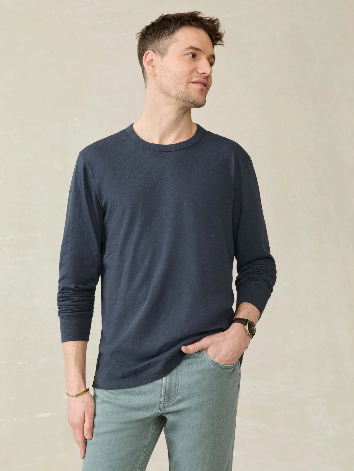 A man wearing a faherty navy long-sleeve shirt and light blue jeans against a beige background.