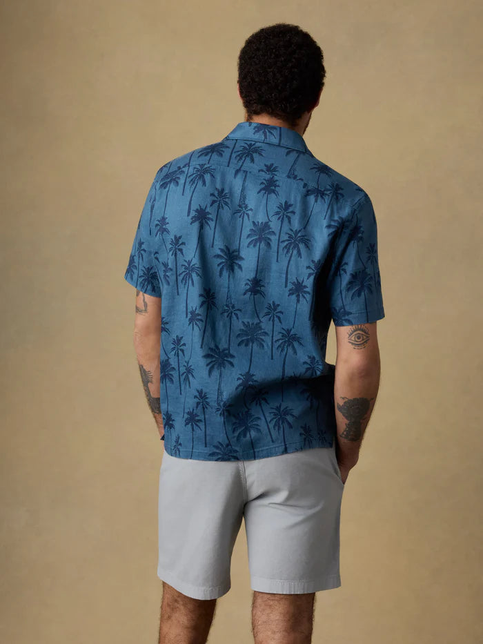 A man wearing a blue palm tree patterned shirt and light gray shorts on a beige background.