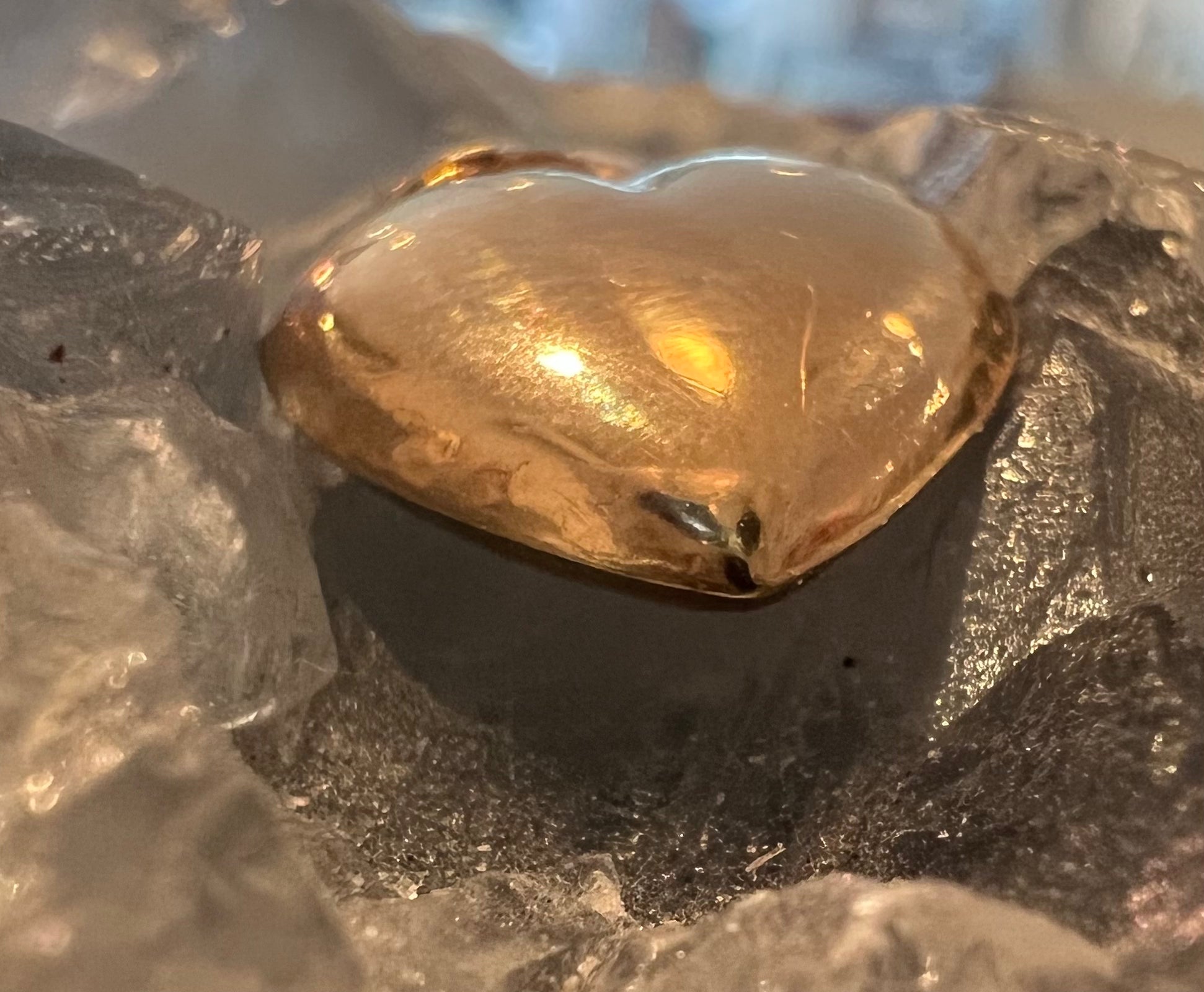 An organic solid 14k gold heart-shaped pendant, from the bottom, demonstrating the 3D dimension of the pendant. On a celestite crystal.  