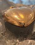 An organic solid 14k gold heart-shaped pendant, from the bottom, demonstrating the 3D dimension of the pendant. On a celestite crystal.  