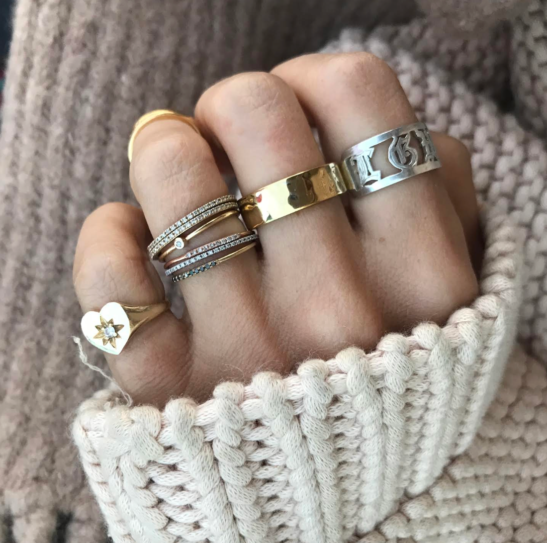 Hand wearing multiple rings with a chunky sweater background. The Charlotte Heart Starburst ring is on the pinky finger. 