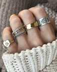 Hand wearing multiple rings with a chunky sweater background. The Charlotte Heart Starburst ring is on the pinky finger. 
