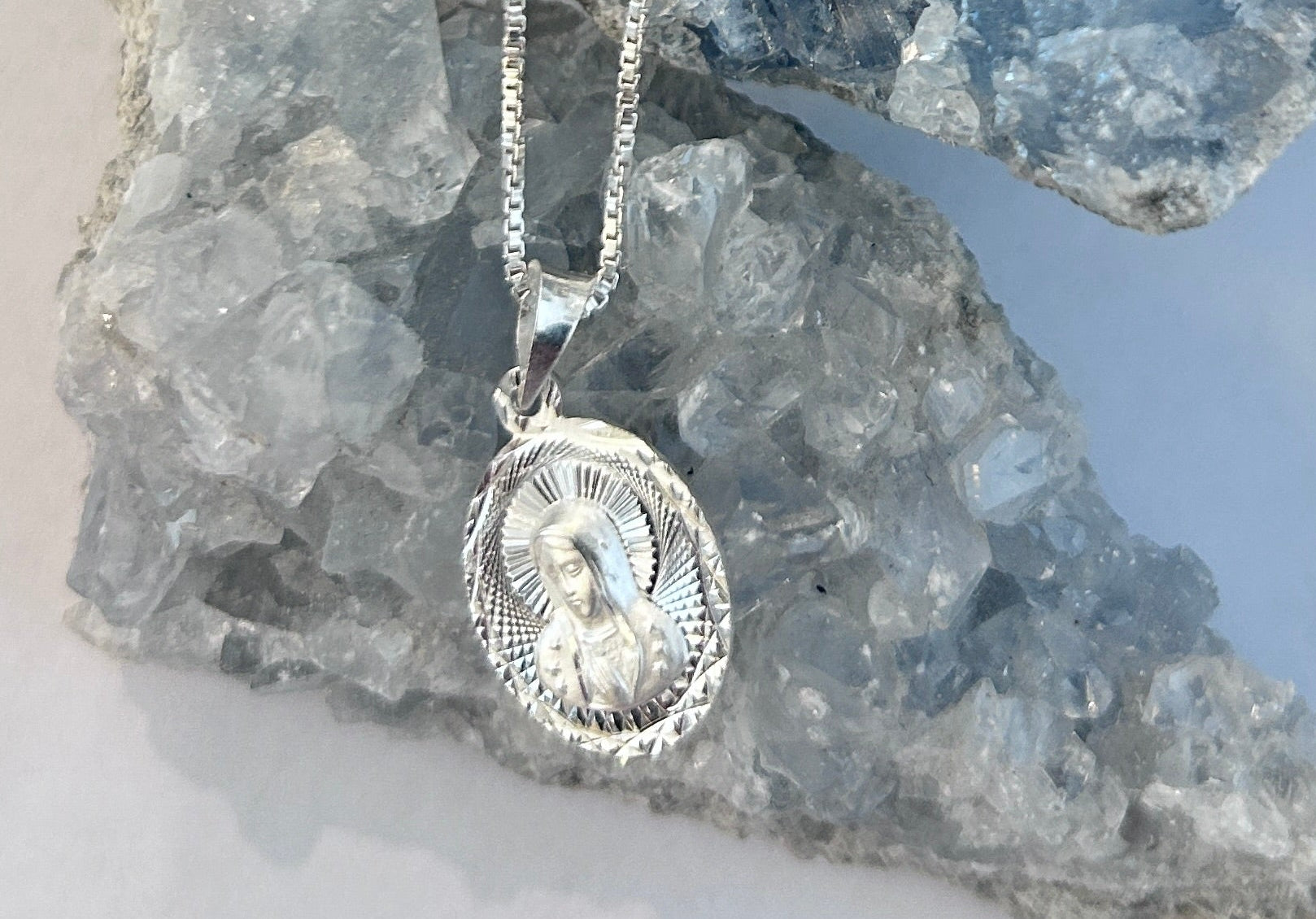 Sterling Silver Our Lady of Guadalupe highly-polished circular pendant, on an 18 inch box chain. Set on a crystal background. 