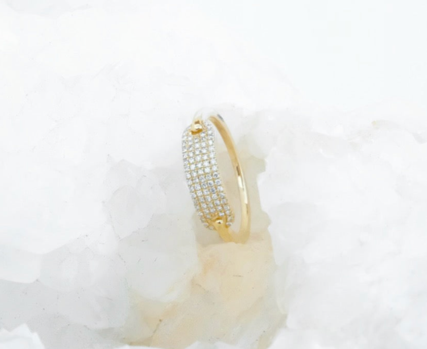 A 14k gold ring with a pavé-set row of clear diamonds, displayed on a textured white crystal surface.