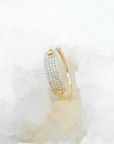 A 14k gold ring with a pavé-set row of clear diamonds, displayed on a textured white crystal surface.
