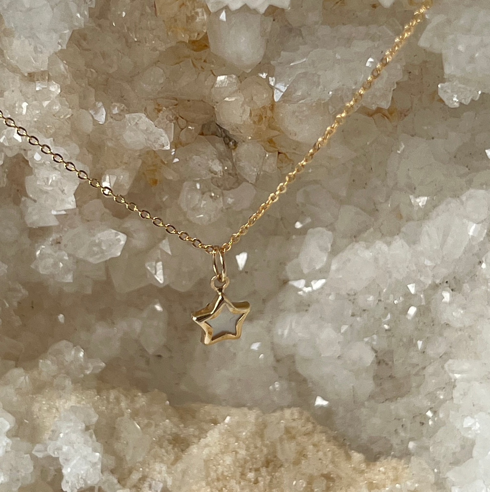 A 14k yellow gold petite mother of pearl star pendant necklace on an 16-inch classic cable chain, displayed against a crystalline rock background.