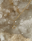 A 14k yellow gold petite mother of pearl star pendant necklace on an 16-inch classic cable chain, displayed against a crystalline rock background.