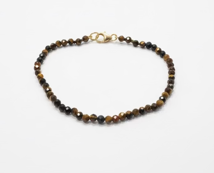 A brown and black beaded Tiger's ye bracelet, with a small gold-filled clasp. Against a white background. 